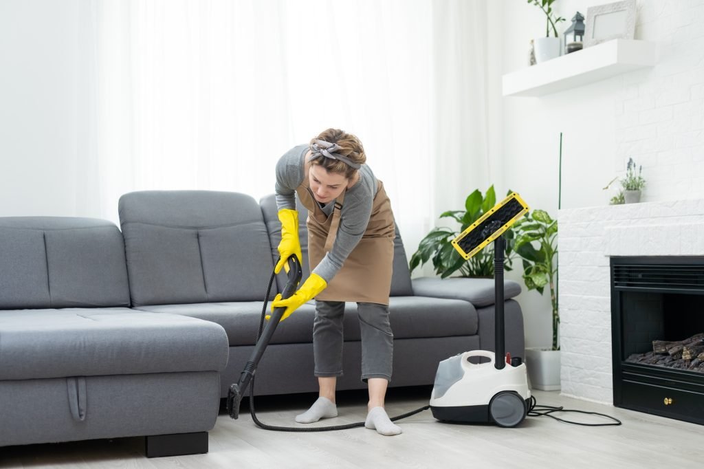 Woman cleaning couch with vacuum cleaner at home