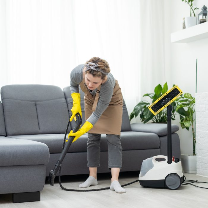Woman cleaning couch with vacuum cleaner at home